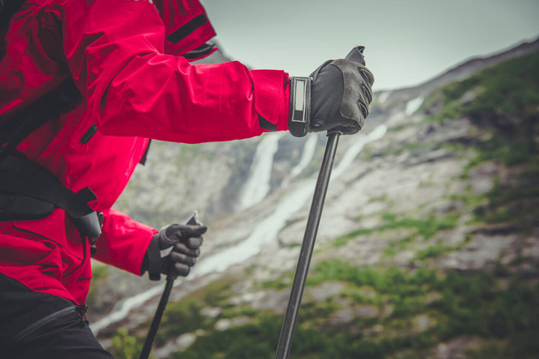 A Person in Red Winter Jacket and Protective Gloves Hiking With Poles and Backpack Among the Scenic Mountain Views. Outdoor Activities Theme. - Foto, Imagen