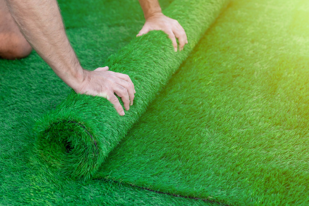 Selective focus on a man's hands unrolling a roll of artificial turf. Easy laying of artificial green grass - Photo, image