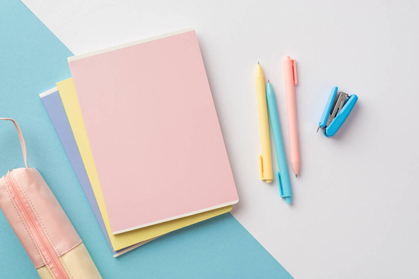 Back to school concept. Top view photo of colorful school supplies stack of copybooks pens mini stapler and pink pencil-case on bicolor blue and white background - Foto, immagini