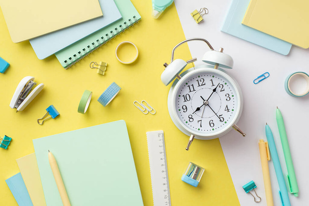 Back to school concept. Top view photo of alarm clock diaries sharpener ruler pens binder clips adhesive tape and stapler on bicolor yellow and white background - Foto, afbeelding