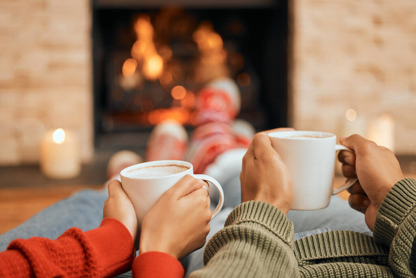 Hot cocoa just tastes better this time of year. Closeup shot of a couple having warm drinks while relaxing by a fireplace at home - Foto, immagini