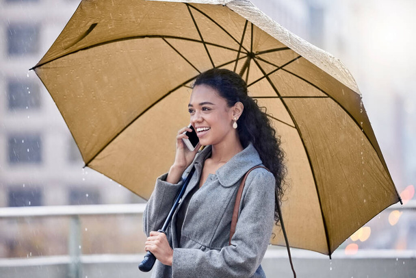Im caught in the rain. a young woman holding an umbrella while on a call in the rain - Fotografie, Obrázek