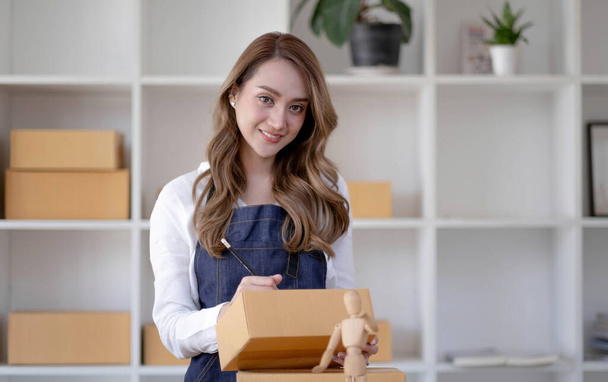 Startup SME small business entrepreneur SME or freelance Asian woman using a laptop with box, Young success Asian woman with her hand lift up, online marketing packaging box and delivery, SME concept - Photo, Image