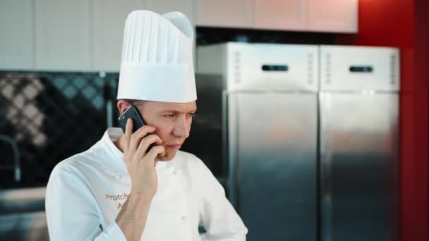 The chef is talking on the phone in kitchen. - Filmagem, Vídeo