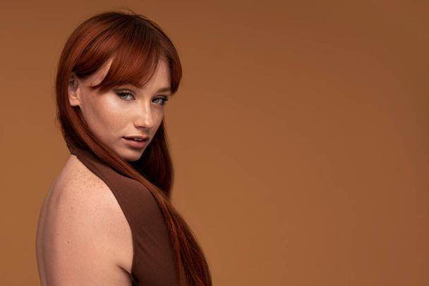 Ginger beauty girl with natural freckles, long healthy hair and fringe. Attractive red head woman posing in studio, looking at the camera. A lot of copy space - Foto, immagini