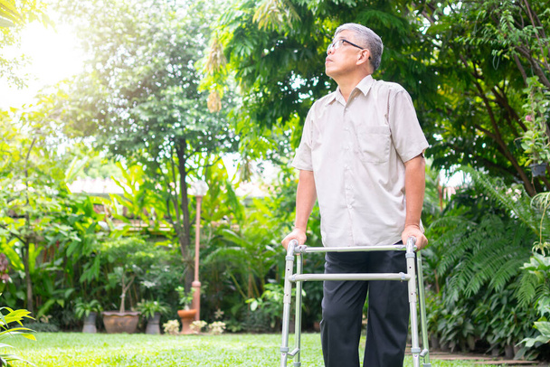 Iloinen vanha aasialainen mies kävelee takapihalla kävelijällä. Onnellisen eläkkeelle siirtymisen käsite Hoitaja ja säästöt ja vanhempi sairausvakuutus - Valokuva, kuva