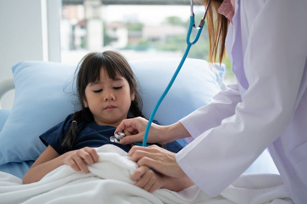 Asian woman pediatrician doctor hold stethoscope for exam a little girl patient and heck heart lungs of kid, Good family doctor visiting child at home, Healthcare and medicine for childhood concept. - Фото, изображение