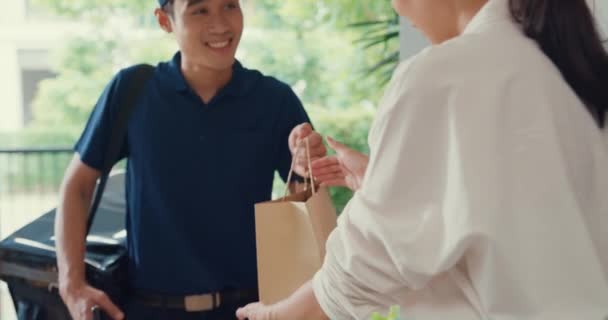 Close-up Young Asian delivery man in blue navy uniform carry case box knock door home online shopping to woman in front of the door and lady sign accept paper bag on smartphone at house concept. - Filmagem, Vídeo