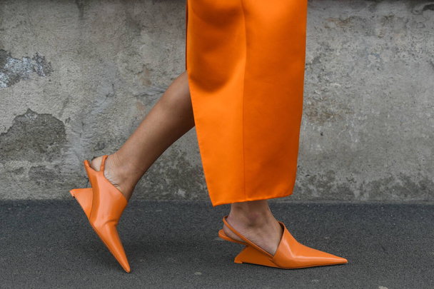 MILAN, ITALY - FEBRUARY 24, 2022: Elegant woman wearing orange long dress, black bag and white gloves. - Фото, изображение