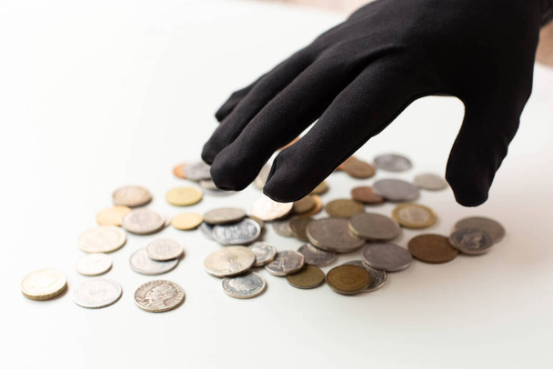 A hand in a black glove hung over different coins. The theme of theft and economic crime. - Zdjęcie, obraz
