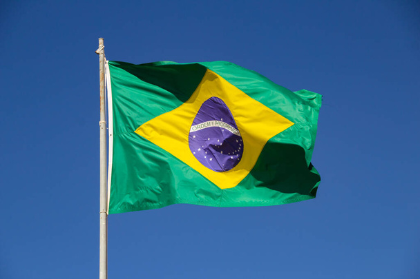 Brazilian flag flying and fluttering in the wind with blue sky in the background. - Foto, Imagen