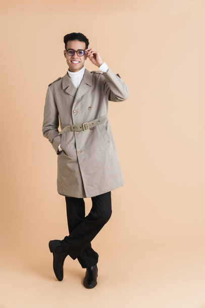 Young middle eastern man wearing coat smiling and looking at camera isolated over beige background - Fotó, kép