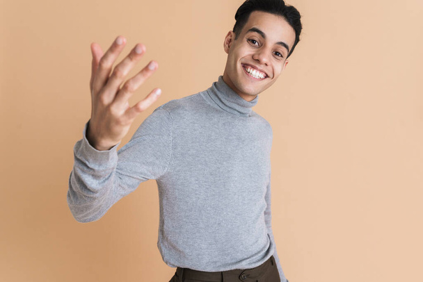 Young middle eastern man gesturing and smiling at camera isolated over beige background - Foto, Imagem