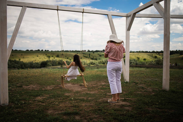 Vrolijke dame in witte jurk leunend terug in haar swing in zonnige gouden platteland. - Foto, afbeelding