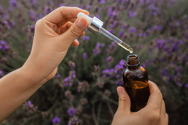 Dropper with lavender essential oil over a bottle in a blooming field, close-up. - Φωτογραφία, εικόνα