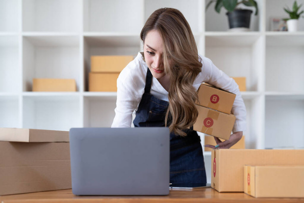 Portrait young attractive asia female owner startup business look at camera work happy with box at home prepare parcel delivery in sme supply chain, procurement, omnichannel commerce online concept - 写真・画像
