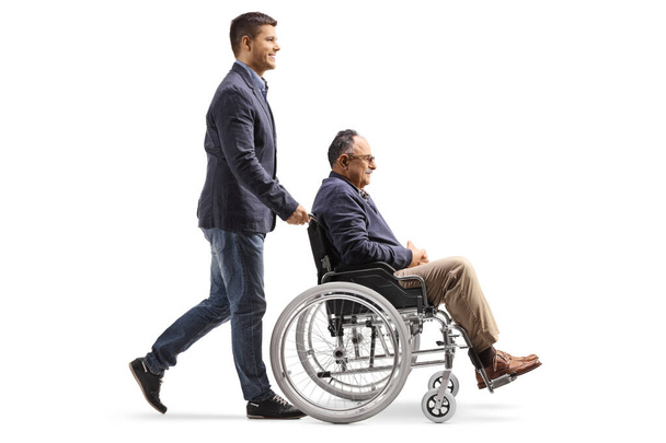 Full length profile shot of a son walking and pushing a mature man in a wheelchair isolated on white background  - Foto, Bild