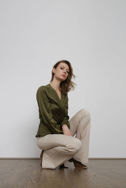 Serie of studio photos of young female model wearing green silk blouse and basic beige flared trousers - Фото, изображение