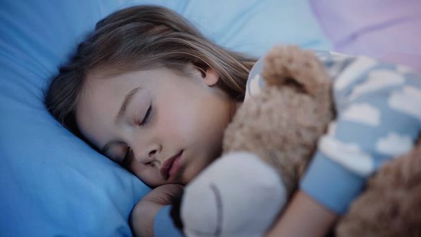 Preteen child hugging blurred teddy bear while sleeping on bed  - Foto, Imagem