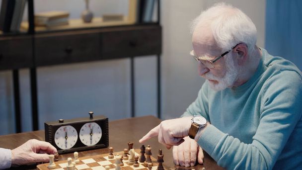 elderly man pointing at chessboard near timer and friend  - Foto, Imagem