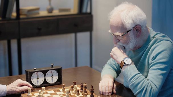 pensive man looking at chessboard while gaming with senior friend at home - Foto, Imagen