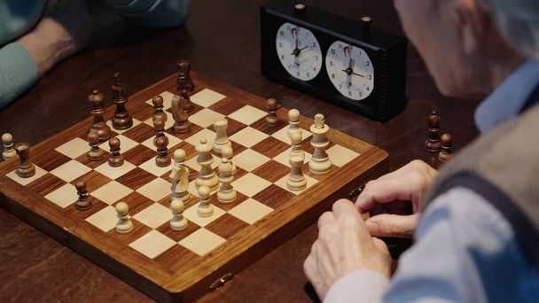 cropped view of senior men playing chess near blurred timer - 写真・画像