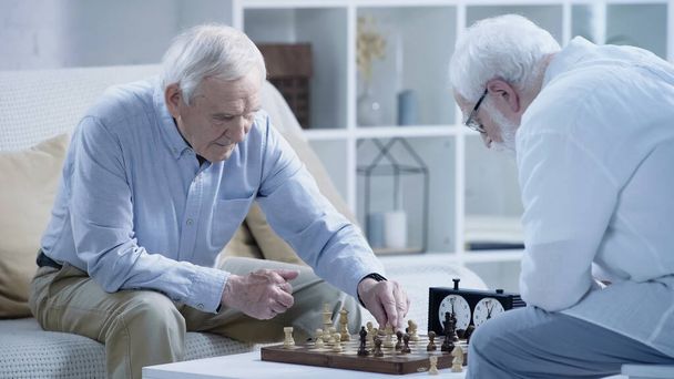 grey haired man playing chess with senior friend in living room - Foto, immagini