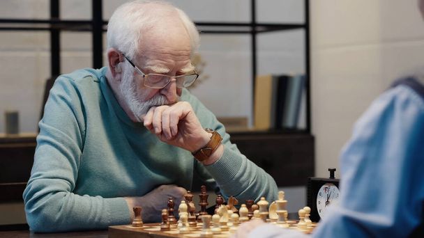senior thoughtful man playing chess with friend in living room - Φωτογραφία, εικόνα