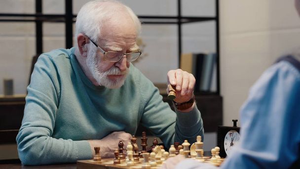 senior bearded man moving chess figure while gaming with friend at home - Zdjęcie, obraz