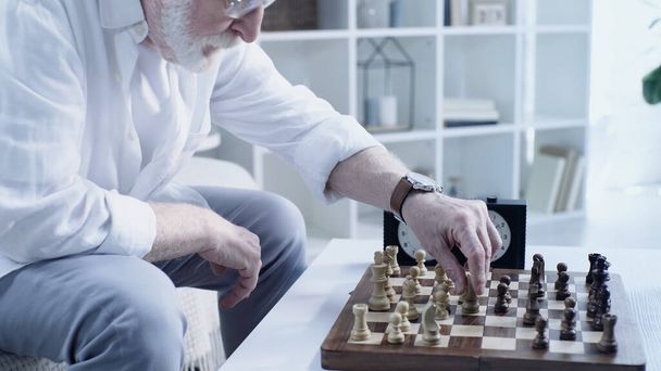частковий вид на старшого бородатого чоловіка, який грає в шахи вдома у вітальні
 - Фото, зображення