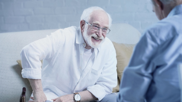 cheerful senior man in eyeglasses laughing near blurred friend at home - Fotó, kép
