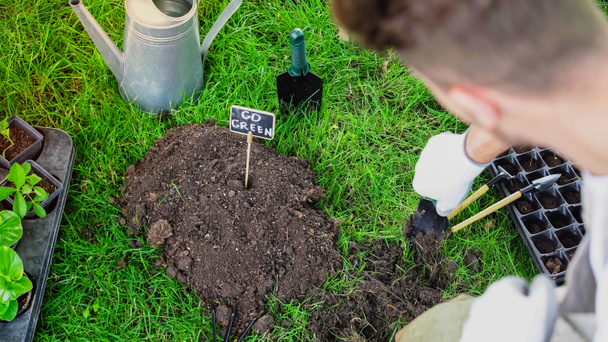 Blurred gardener holding shovel near soil and board with go green lettering in garden  - 写真・画像