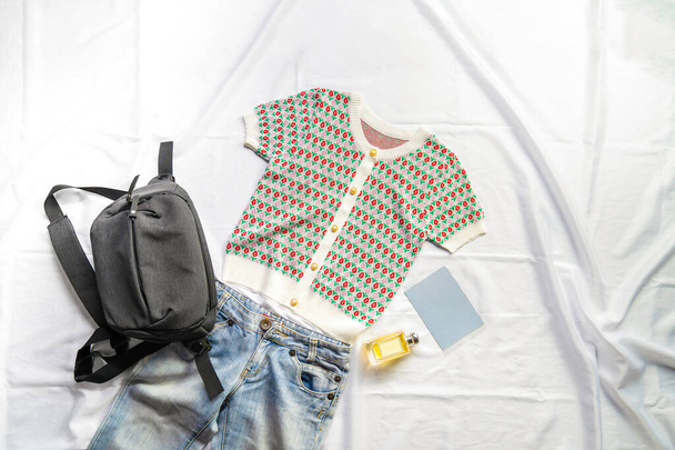 Green crop top with a tulip pattern and light colored jeans are paired with a black bag on the white backdrop. It's suitable for a clothing advertisement on social media. - Foto, immagini