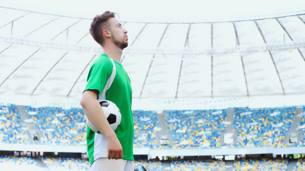 side view of young football player in green t-shirt breathing while holding ball - Foto, Imagen
