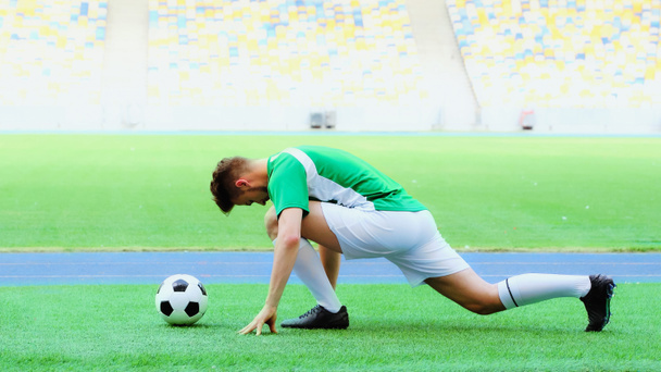 young football player in uniform stretching legs on green grass bear soccer ball  - Foto, Imagen