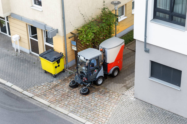 Top above view of small sweeping vacuum cleaner machine equipment removing dust rubbish city street sidewalk paved road near apartment condo building. Special municipal sweeper vehicle cleaning town. - Fotó, kép