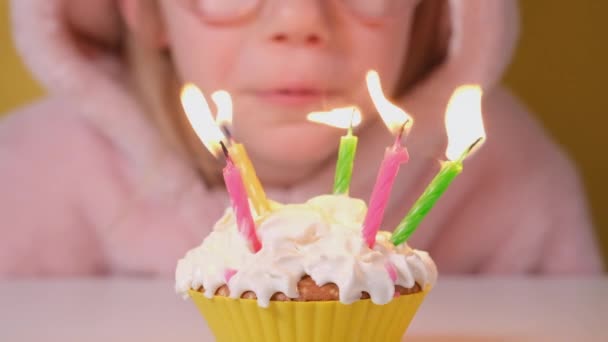 Happy child girl in pink Overalls blowing out five candles on birthday cake at party. Close up on girl face in glasses. Slow motion happy birthday video banner - Filmati, video