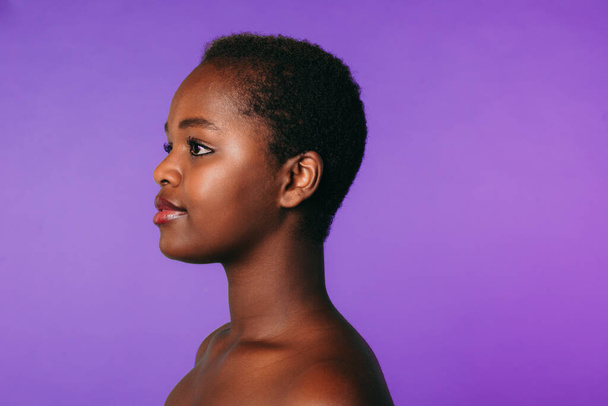 Side view of african-american woman posing while representing spa service against purple background. Makeup, curly hair. White background. Natural beauty - Foto, immagini
