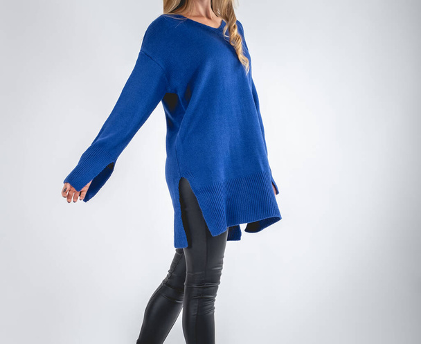 Blonde model girl without face in blue sweater and black bright leatherette pants in light gray background  - Foto, Imagem