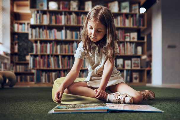 Child solving riddle in book in school library. Primary school pupil is involved in book with riddles. Smart girl learning to solve problems. Benefits of everyday practice. Child curiosity - Fotoğraf, Görsel