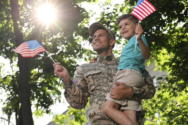 Soldier and his little son with American flags outdoors, low angle view. Veterans Day in USA - Photo, image