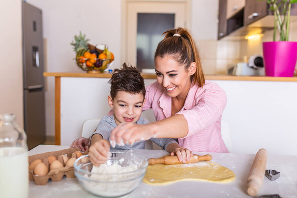 Šťastná milující rodina spolu připravuje pekárnu. Matka a syn chlapec jsou vaření sušenky a baví v kuchyni. Domácí jídlo a malý pomocník. - Fotografie, Obrázek