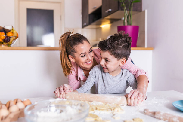 Glücklich liebende Familie bereiten gemeinsam Backwaren zu. Mutter und Sohn kochen Plätzchen und haben Spaß in der Küche. Selbstgemachtes Essen und kleine Helfer. - Foto, Bild