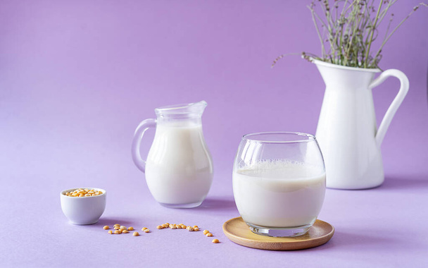 Vegan healthy pea milk in glass and jar, pea seeds and white jug with lavender. Lilac background. Copy space. Healthy food concept - Photo, Image