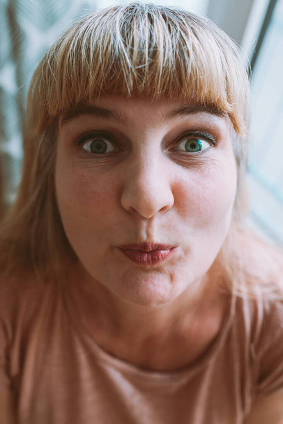Portrait of funny blonde woman with bangs, eyes wide open, lips in kiss, wide lens effect. funny woman face distorted angle - Φωτογραφία, εικόνα