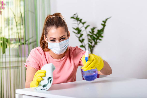 Woman with protective glove and facial mask.Health protection. Hands with yellow gloves.She sprinkling disinfectant and cleaning the table. Stay safe. - 写真・画像
