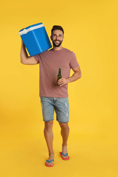 Happy man with cool box and bottle of beer on yellow background - 写真・画像