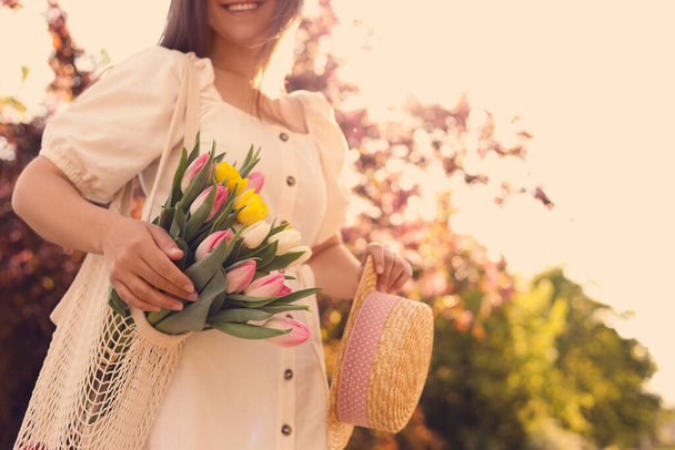 Young woman with bouquet of tulips and hat in park on sunny day, closeup. Space for text - Valokuva, kuva