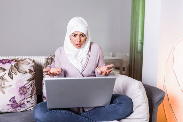 Портрет жінки-мусліма виглядає сердитим під час роботи над ноутбуком. Молода арабка має відео-дзвінок через лептоп вдома.. - Фото, зображення