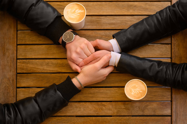 Lovely couple with coffee holding hands together at wooden table, top view. Romantic date - Photo, image